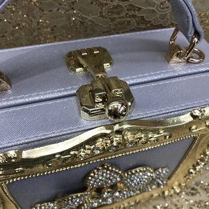 Close-up of lilac box clutch with gold metal frame, crystal inlay and vintage lock