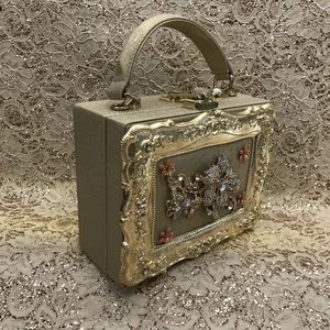 Detailed side view of gold evening bag with floral rhinestone and pink flower accents