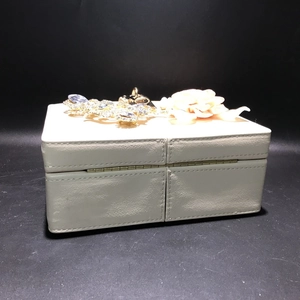Détail de la pochette en cuir PU crème avec fleurs en satin et décorations en strass