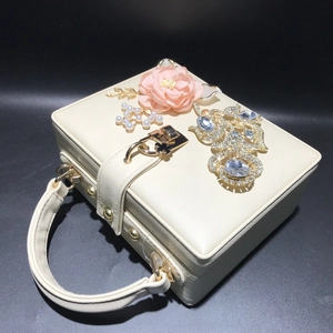 Vue détaillée d'une pochette blanche avec fleur en soie rose et ornements dorés sertis de strass