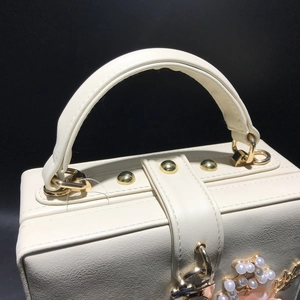 Détail du sac boîte en cuir blanc avec rivets dorés et pendentif perle fleurie