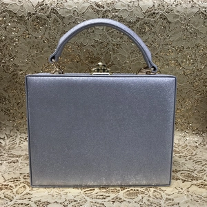 Detail of silver-purple square box clutch bag with gold metal clasp and top handle