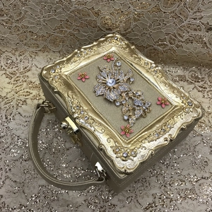 Close-up of gold evening clutch with sparkling rhinestones and pink enamel floral details