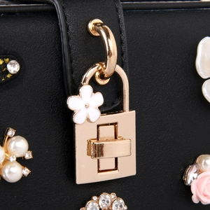 Détail de sac en cuir noir avec fermoir doré, perles et décorations florales en cristal