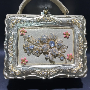 Close-up of gold embossed evening bag with rhinestone flower and pink enamel details