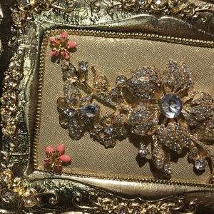 Close-up of golden floral clutch detail with rhinestones and pink enamel flowers
