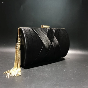 Detail of black silk evening clutch featuring gold chain tassel and metal clasp closure