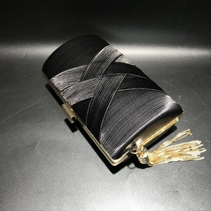 Detailed close-up of a black silk evening clutch featuring gold metal tassels and clasp
