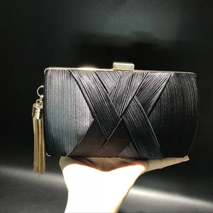 Detail of black silk pleated evening clutch with gold metal frame and long tassel chain