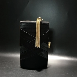 Detail of black silk woven evening clutch featuring long gold tassel and metal clasp