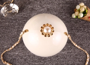 Détail d'une pochette sphérique blanc cassé avec fermoir fleur perlée et chaîne dorée