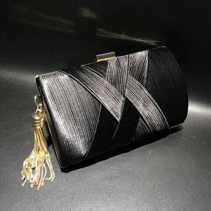 Detail of black silk evening clutch featuring pleated texture and gold chain tassels