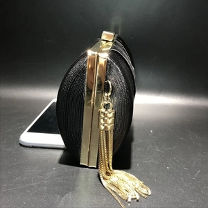 Detail of silk textured black evening bag with gold metal frame and hanging tassel