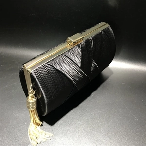 Detail of black pleated satin evening clutch with gold metal frame and long tassel chain