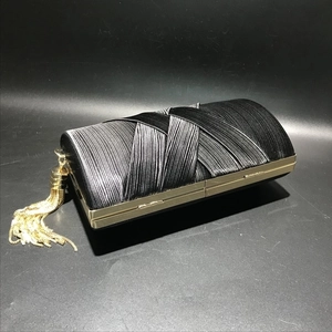 Detail of black silk evening clutch featuring pleated fabric and golden tassel accents