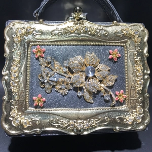 Detailed view of luxury evening bag featuring crystal flower clusters and gold relief frame