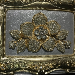 Close-up of a floral golden alloy brooch with sparkling rhinestones on a gray backdrop