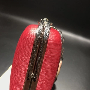 Detail of red textured leather clutch with vintage engraved metal frame for evening wear