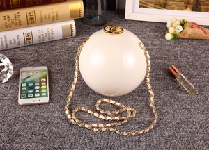 Sac de soirée sphérique blanc perle avec chaîne dorée présenté dans un décor lifestyle