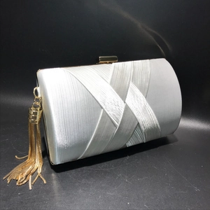 Detail of silver satin evening clutch with gold tassel and elegant ribbon overlay texture