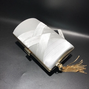 Detail of white silk evening clutch bag with woven texture and gold chain tassel accents