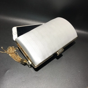 Detail view of woven evening clutch with gold tassels showing phone capacity and dimensions