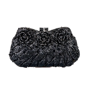 Macro detail of luxury black evening clutch featuring three 3D crystal roses and metal texture