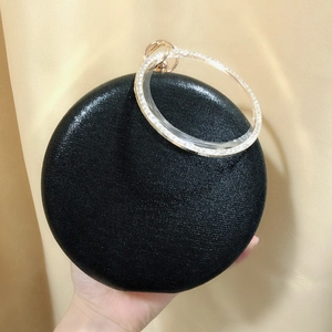 Detail of round black evening clutch with rhinestone bracelet handle held in hand
