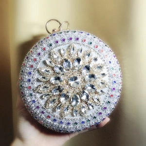 Detail of round silver evening clutch with colorful gemstones and golden ring handle