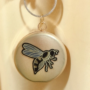 Macro view of gold satin evening bag with bee embroidery and crystal ring handle