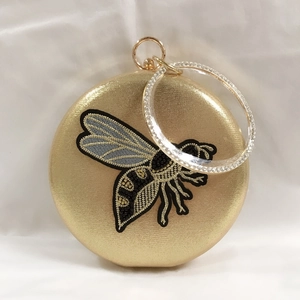Macro detail of golden round evening bag with bee embroidery and crystal ring handle