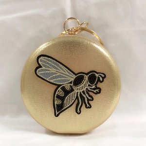 Detail of round gold evening clutch with bee embroidery and metal ring handle