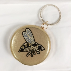 Detail of round evening clutch featuring bee embroidery and a rhinestone ring handle
