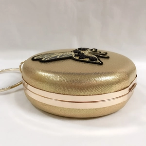 Detail of champagne gold round evening bag with bee embroidery and rhinestone ring handle
