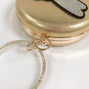 Detail of golden round clutch with bee embroidery and sparkling rhinestone ring handle