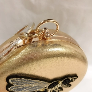 Detail of a gold oval evening clutch with bee embroidery and metal ring handle