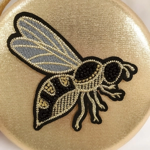 Macro shot of bee embroidery with metallic threads and black beads on gold clutch