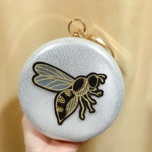Silver round evening clutch with gold bee embroidery and ring handle held by hand