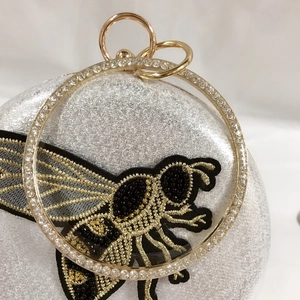Detail of bee embroidery on a silver sequin evening bag with a rhinestone ring handle