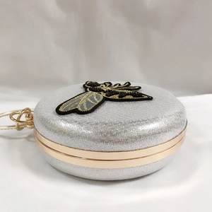 Detail of silver glitter evening clutch featuring 3D bee embroidery and gold metal frame