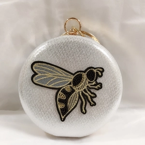 Macro view of silver glitter clutch featuring gold bee embroidery and metal ring handle