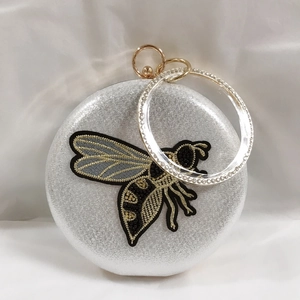 Macro shot of silver evening bag with bee embroidery and crystal ring handle