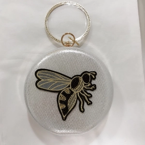 Detailed view of silver glitter evening bag with embroidered bee and rhinestone ring handle
