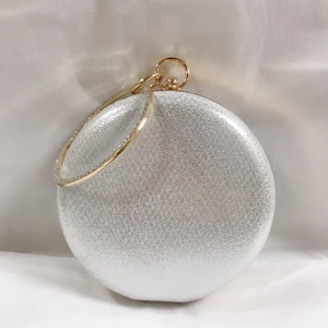 Detail of round silver evening clutch bag featuring a gold ring handle on a soft silk background