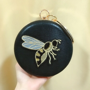 Close-up of black PU evening clutch featuring detailed bee embroidery and gold ring handle