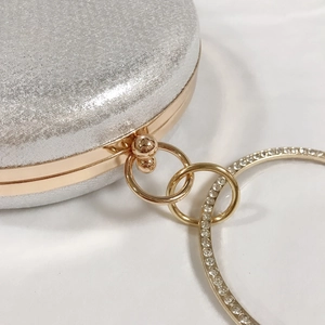 Détail de pochette de soirée à paillettes argentées avec cadre doré et poignée anneau strass