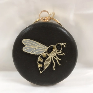 Detail of round black evening bag featuring gold bee embroidery and metal ring handle