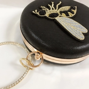 Detail of bee bead embroidery and sparkling rhinestone ring handle on black satin clutch bag