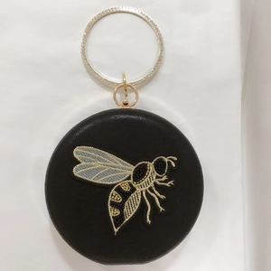 Macro shot of circular evening bag featuring honeybee embroidery and crystal ring handle