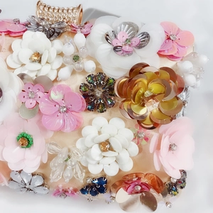 Close-up of champagne satin clutch with 3D sequin flowers and diamond-studded clasp